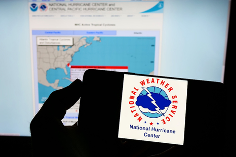 Person holding smartphone with logo of National Hurricane Center NHC on screen in front of website