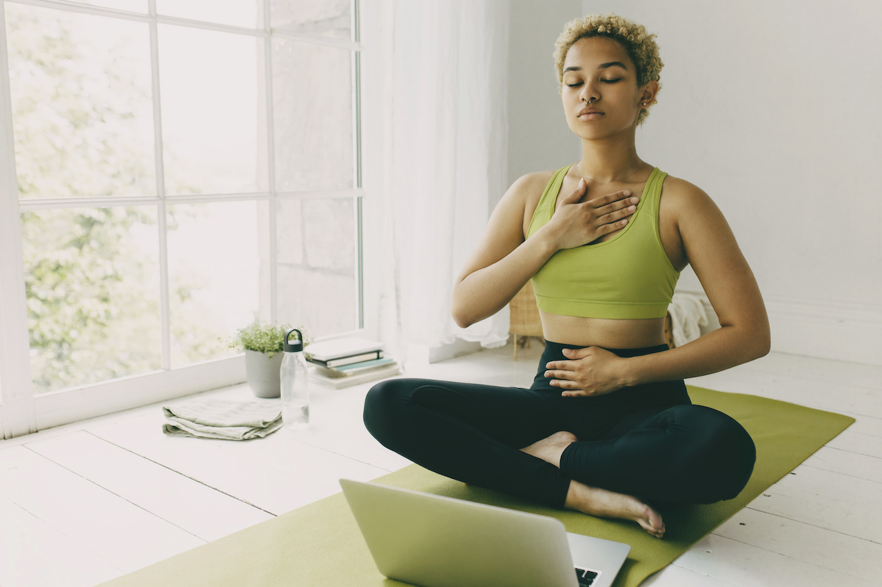 African female yoga teacher having online lesson sitting on green mat in light room showing pranayama techniques jpeg